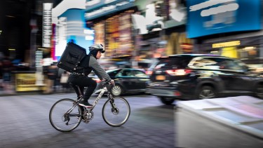 Radzusteller radelt über den im Hintergrund verschommen sichtbaren New Yorker Timesquare